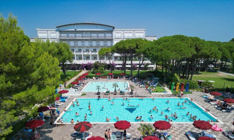 Crowded pool at a resort with red umbrellas and garden.